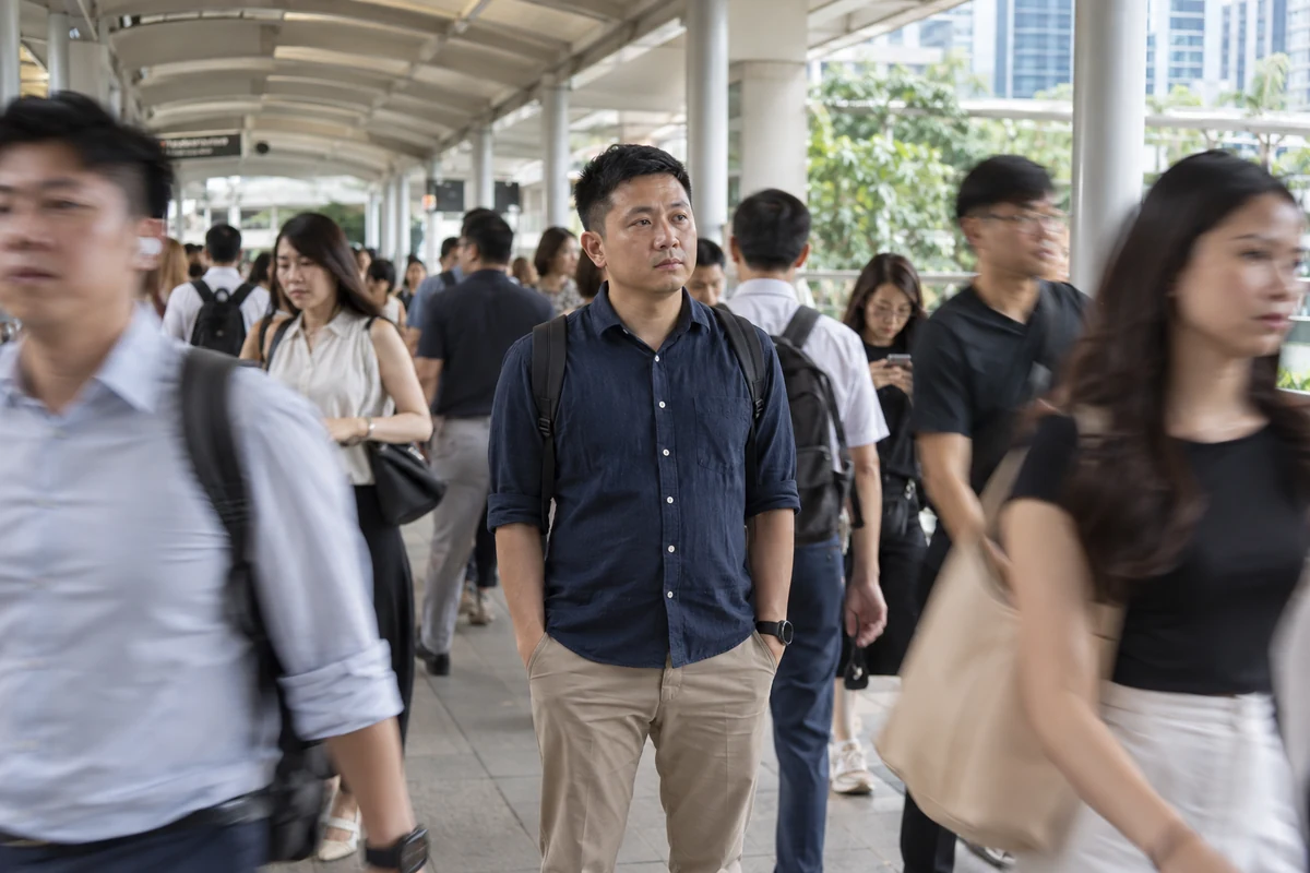 A man stands still while a crowd passes around him on a covered walkway.
